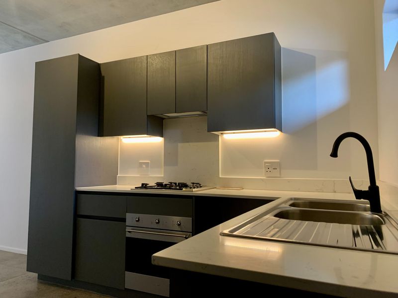 Modern kitchen featuring dark cabinetry, stone countertops, integrated stainless steel appliances, and sleek under-cabinet lighting.