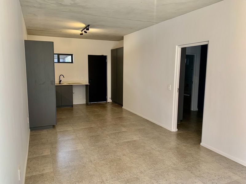An open-plan living and kitchen area featuring modern grey cabinetry, tiled flooring, and an exposed concrete ceiling with track lighting.