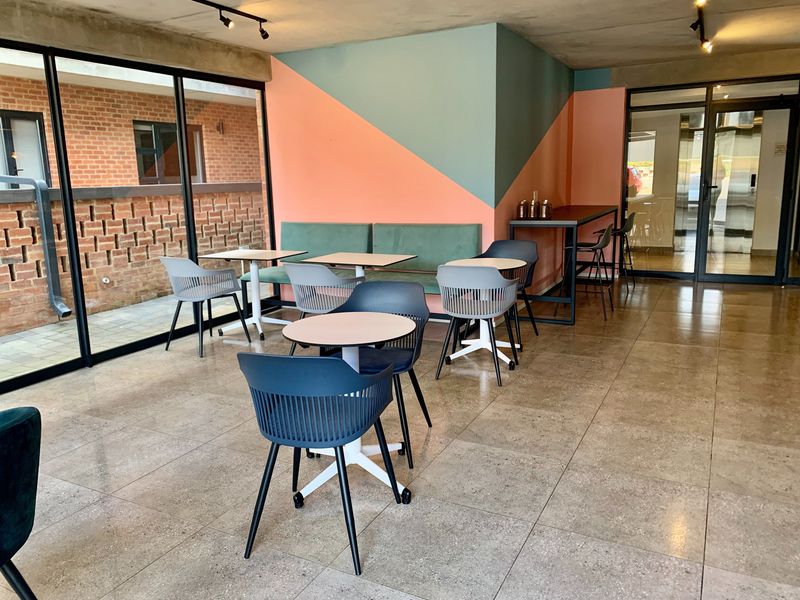 Modern open-plan communal area featuring large glass sliding doors, exposed concrete ceilings, track lighting, and durable tiled flooring with built-in bench seating.