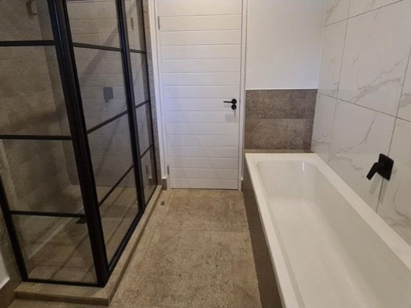 Modern bathroom featuring a walk-in shower with black-framed glass, a built-in bathtub with wall-mounted fixtures, and contemporary marble-effect wall tiling.