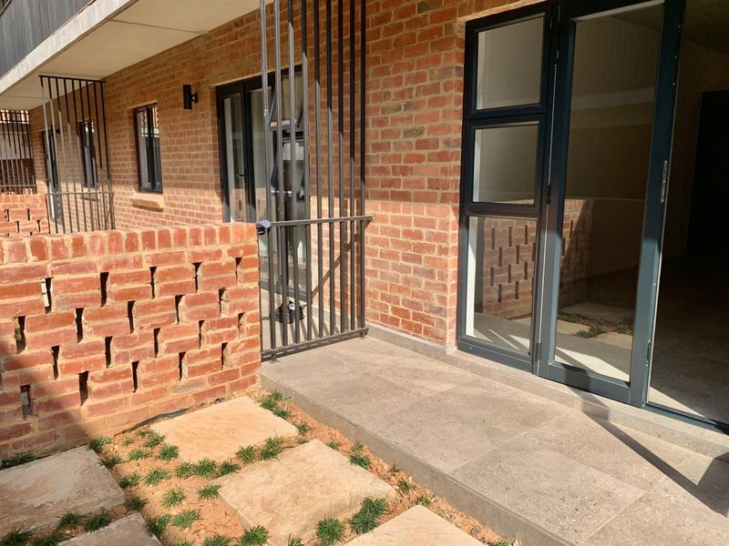 A ground floor patio area featuring exposed brickwork, tiled flooring, and direct access to the interior through aluminium framed glass doors.