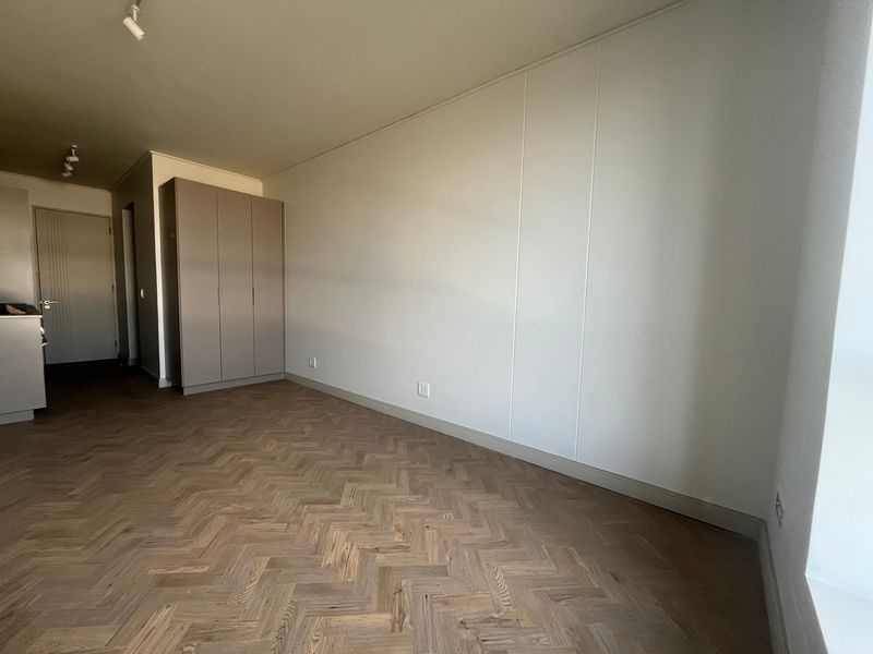 A bright, empty bedroom featuring high-quality herringbone timber flooring, neutral walls, and a modern built-in wardrobe with track lighting.