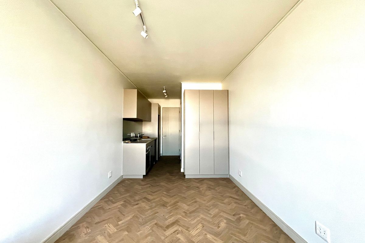 A bright, modern open-plan living space featuring high-quality herringbone timber flooring, track lighting, and sleek built-in cabinetry with integrated kitchen and storage.