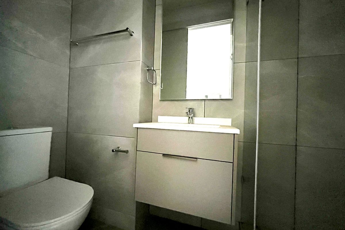 Modern bathroom featuring a wall-mounted vanity, basin, toilet, and a glass-enclosed shower with neutral floor-to-ceiling tiling.