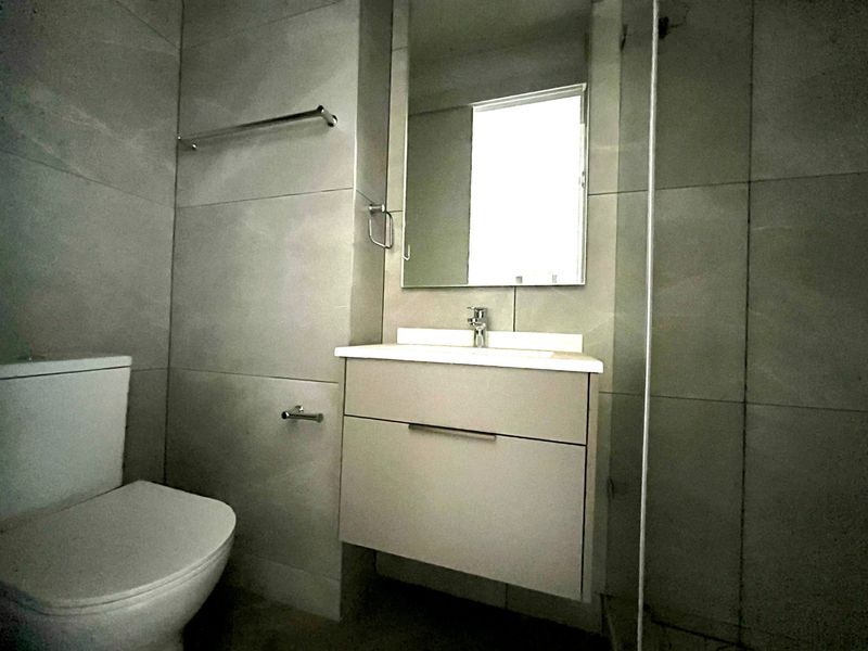 Modern bathroom featuring a wall-mounted vanity, basin, toilet, and a glass-enclosed shower with neutral floor-to-ceiling tiling.