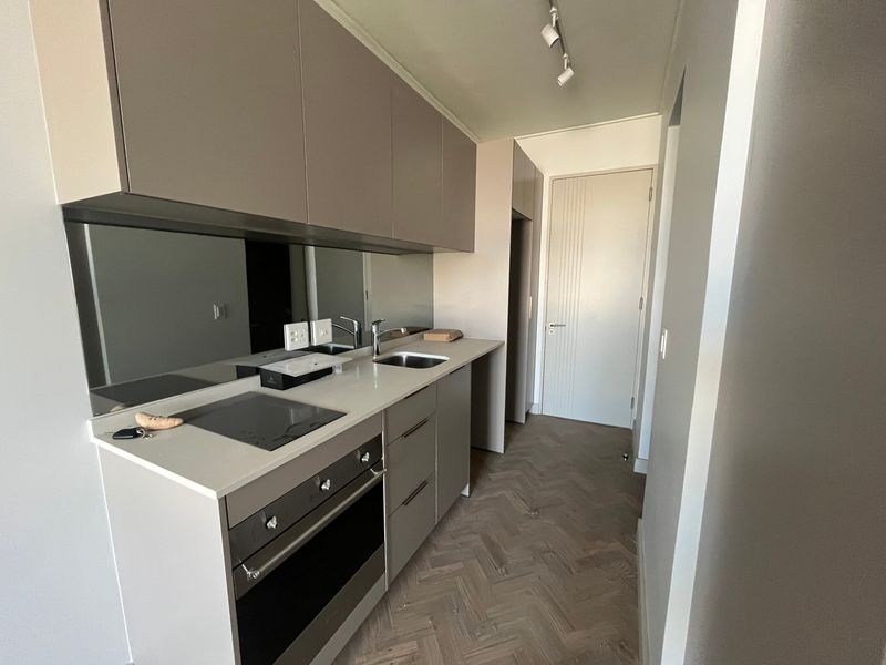 Modern galley-style kitchen featuring sleek handleless cabinetry, a mirrored splashback, integrated oven and hob, and elegant herringbone timber flooring.