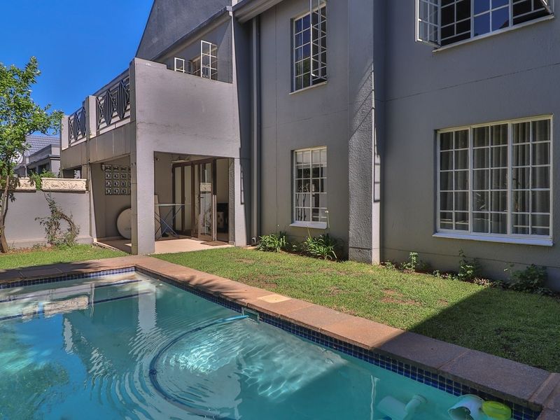 A private rear garden featuring a swimming pool, a covered patio area, and an elevated balcony, set against the rear facade of the apartment building.