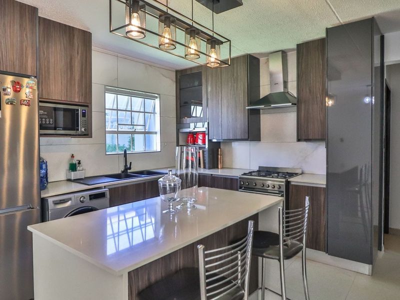 Modern kitchen featuring dark wood cabinetry, stone countertops, a central island, gas hob, extractor fan, and integrated appliances.