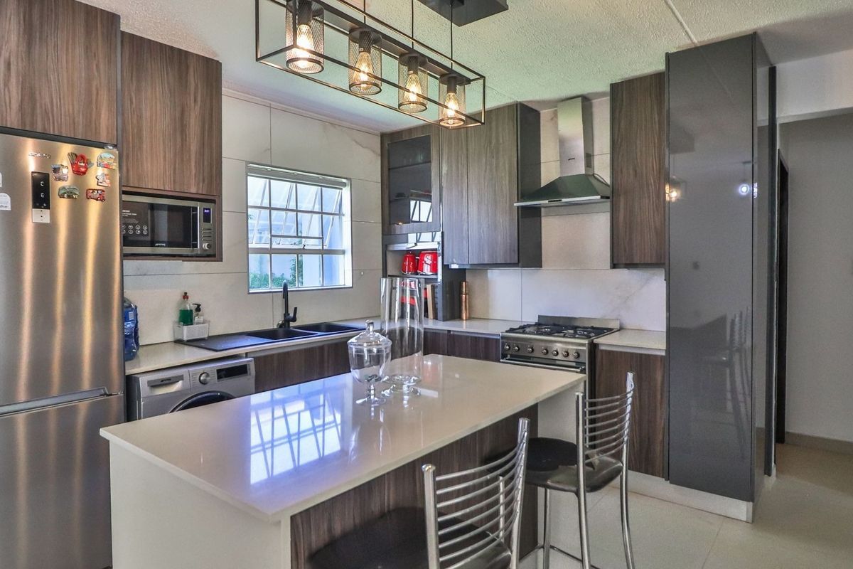 Modern kitchen featuring dark wood cabinetry, stone countertops, a central island, gas hob, extractor fan, and integrated appliances.
