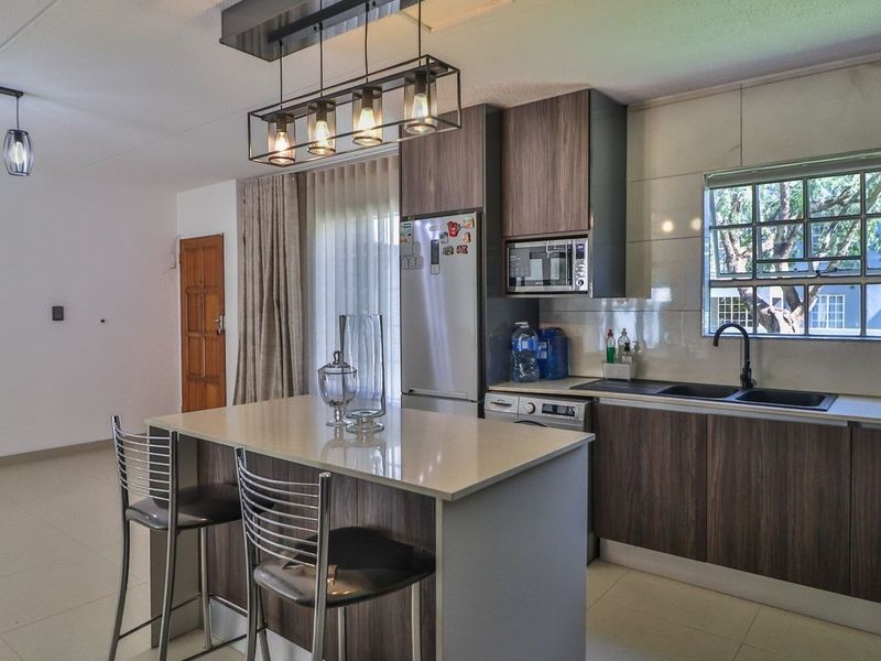 Modern open-plan kitchen featuring a central island with quartz countertops, dark wood cabinetry, integrated appliances, and stylish pendant lighting.