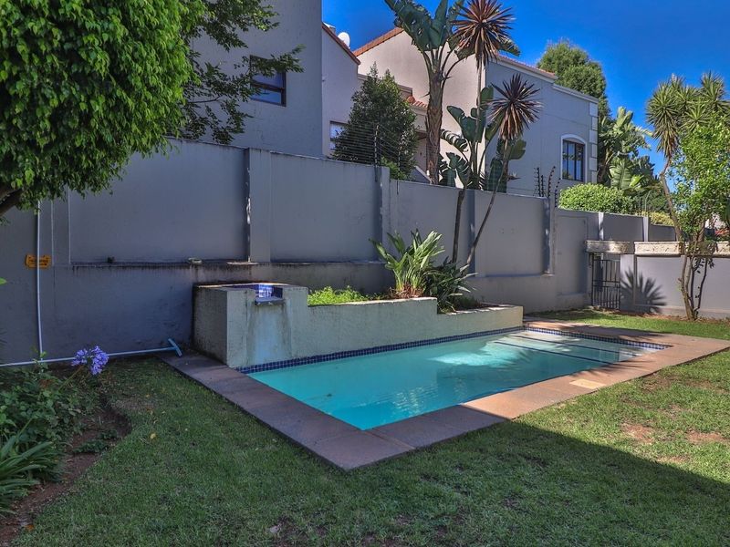 Private backyard featuring a swimming pool with a built-in water feature, surrounded by a lawn and high perimeter walls with electric fencing.