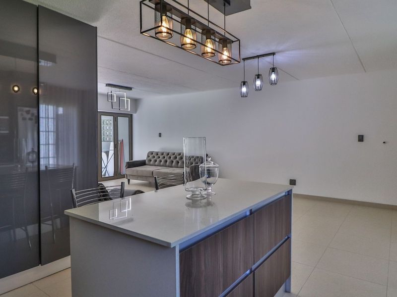 Modern open-plan living area featuring a central kitchen island with stone countertops, sleek cabinetry, and contemporary pendant lighting throughout the space.