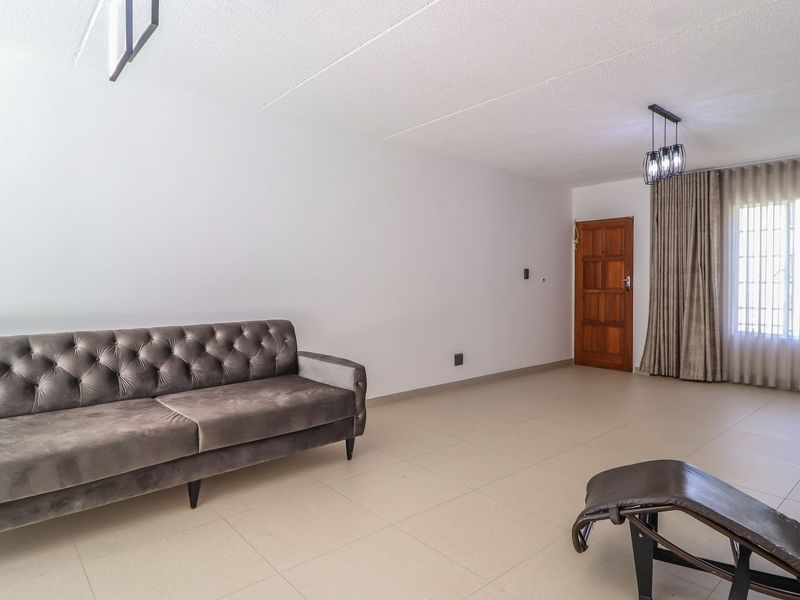 A spacious living area featuring neutral tiled flooring, a textured ceiling, and a timber entrance door with natural light through a window.