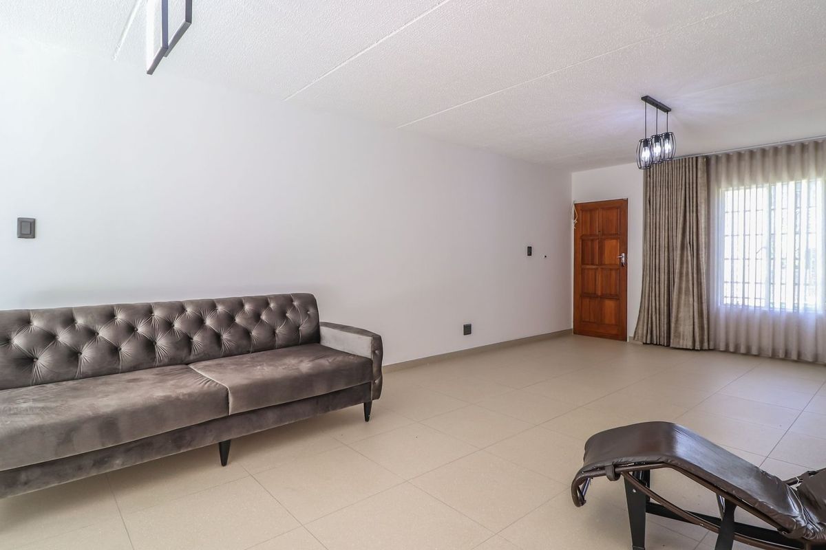A spacious living area featuring neutral tiled flooring, a textured ceiling, and a timber entrance door with natural light through a window.