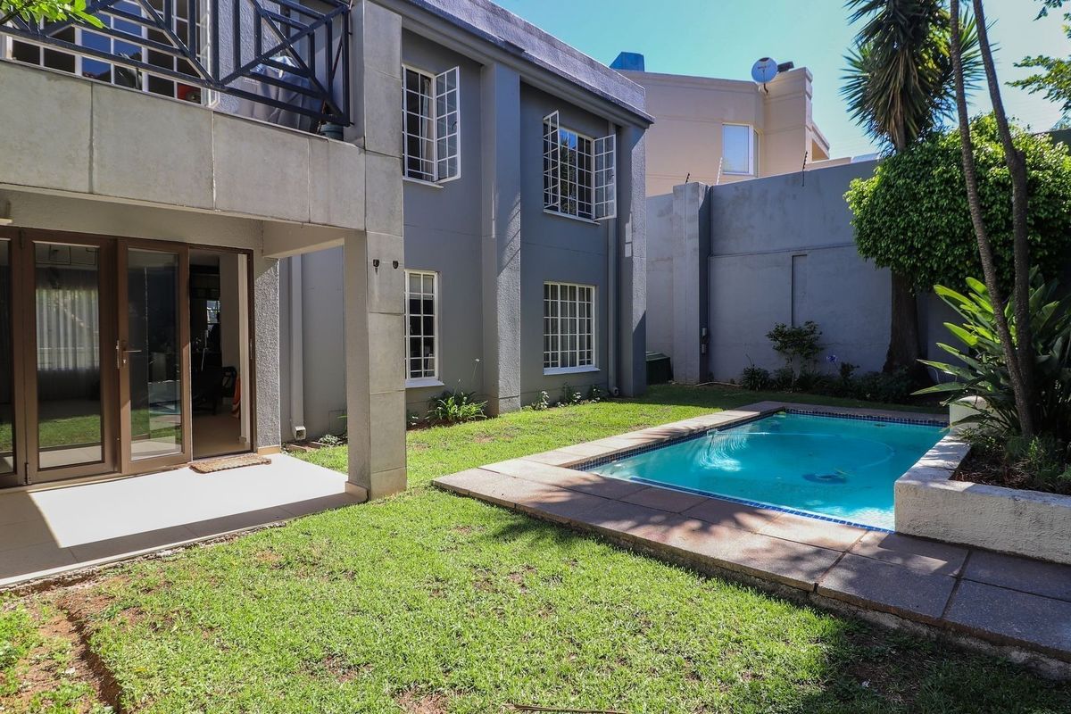 Rear exterior view of the apartment featuring a private garden, a swimming pool, and a covered patio area with an overhead balcony.