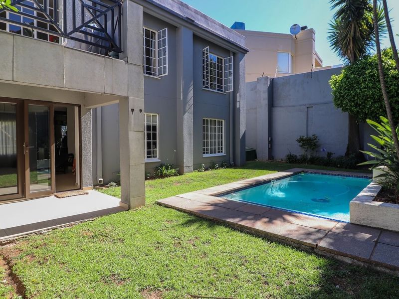 Rear exterior view of the apartment featuring a private garden, a swimming pool, and a covered patio area with an overhead balcony.