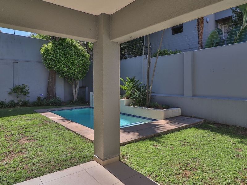 Private outdoor area featuring a swimming pool, raised garden bed, and secure boundary walls with electric fencing, viewed from a covered patio.