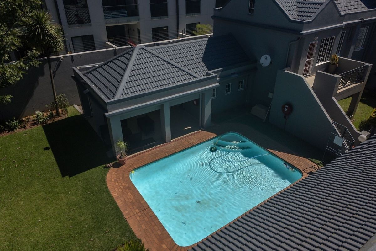 Aerial view of a residential property featuring a swimming pool, paved surround, and a small garden area with a tiled roof structure.