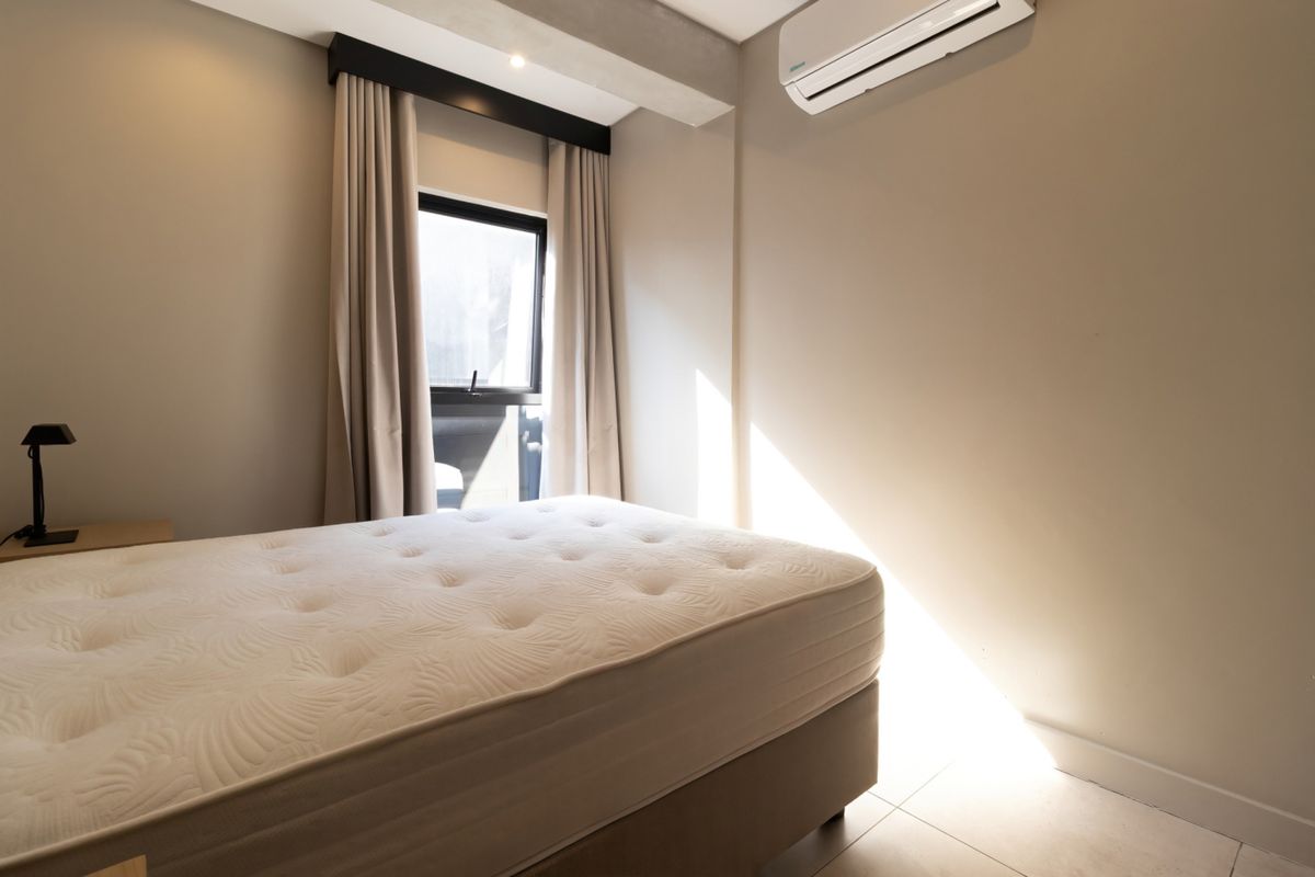 A well-maintained bedroom featuring tiled flooring, a split-system air conditioner, and a window with neutral curtains, offering a clean and functional living space.
