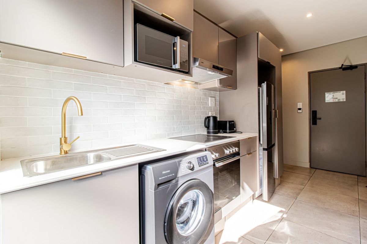 Modern kitchen featuring sleek cabinetry, subway tile backsplash, brass fixtures, and integrated appliances including an oven, hob, and extractor fan.