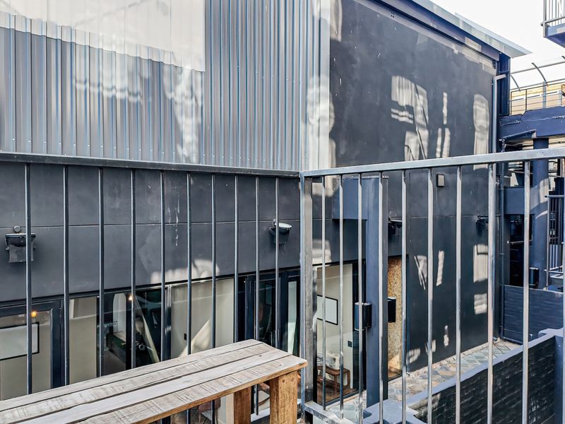 A modern balcony area featuring dark metal cladding, a secure metal railing, and large sliding glass doors providing access to the interior.