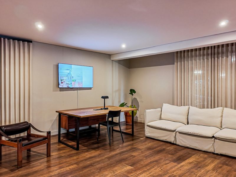 A well-maintained living area featuring warm timber flooring, recessed ceiling lighting, and floor-to-ceiling curtain tracks.