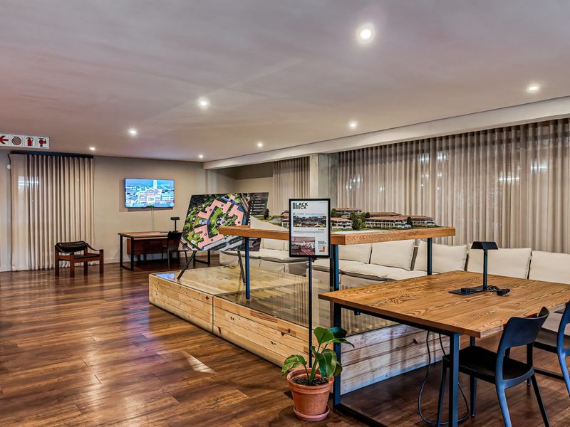A modern, well-lit communal lounge or clubhouse area featuring timber flooring, recessed lighting, and floor-to-ceiling sheer curtains.