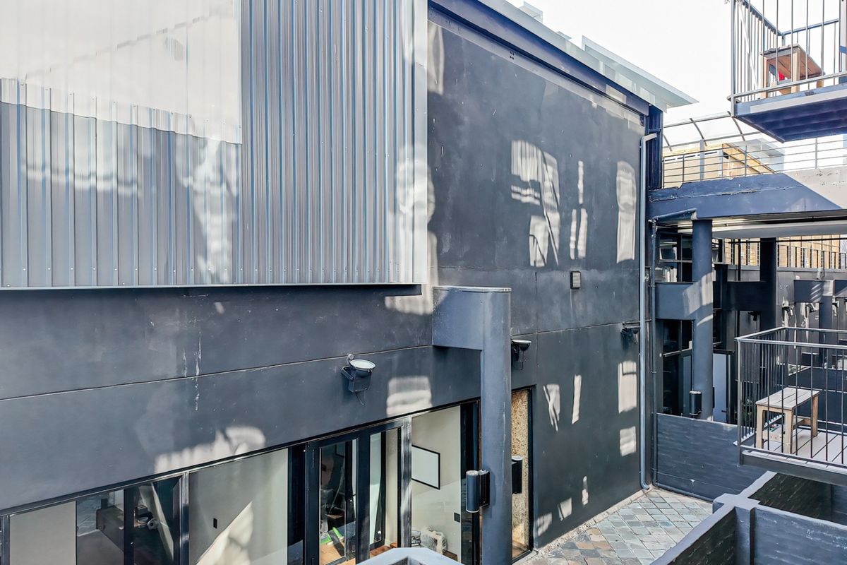 Rear exterior view of the apartment building featuring modern metal cladding, dark painted masonry walls, and a paved courtyard area with metal railings.