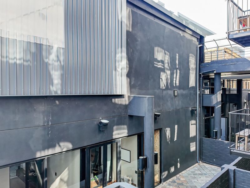 Rear exterior view of the apartment building featuring modern metal cladding, dark painted masonry walls, and a paved courtyard area with metal railings.