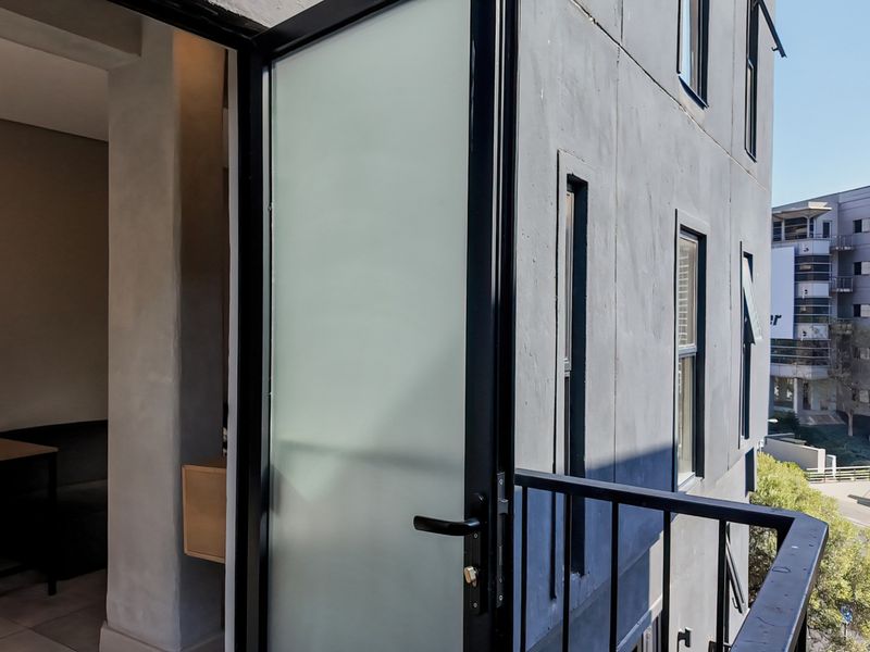 A modern balcony featuring a frosted glass door, black metal railing, and a view of the surrounding urban landscape.
