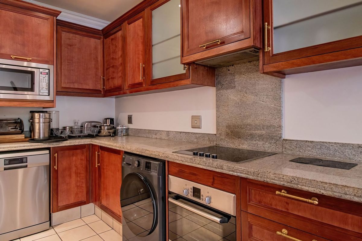 A functional kitchen featuring warm-toned wooden cabinetry, stone countertops, a built-in oven, electric hob, and integrated microwave, providing a classic and practical workspace.