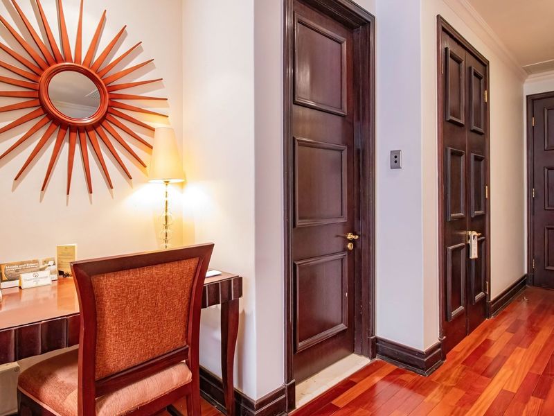 A well-maintained hallway featuring rich hardwood flooring, dark wood panelled doors, and recessed ceiling lighting, creating a warm and inviting transition space.