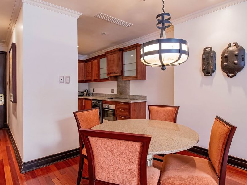 Open-plan dining area featuring warm wooden flooring and a compact, well-equipped kitchen with stone countertops and integrated appliances.