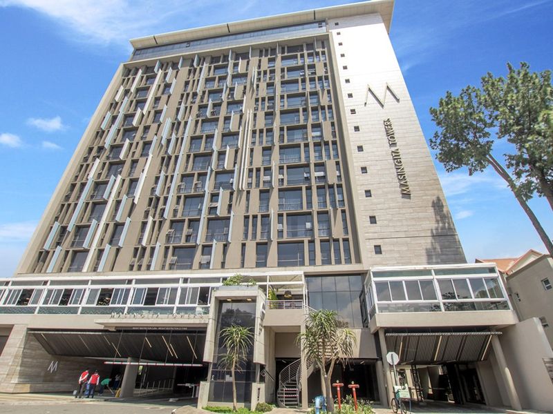 A modern multi-story apartment building facade featuring contemporary architectural design, balconies, and a secure ground-level parking entrance.