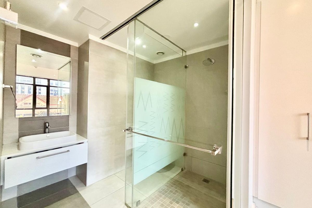 Modern bathroom featuring a wall-mounted vanity with vessel sink, large mirror, and a spacious glass-enclosed walk-in shower with neutral tiling.