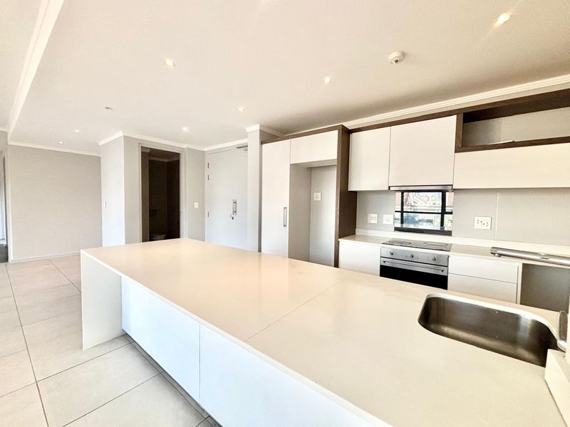 Modern open-plan kitchen featuring sleek white cabinetry, stone countertops, integrated appliances, and recessed lighting in a clean, neutral space.