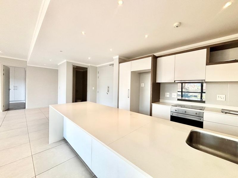 Modern open-plan kitchen featuring a large central island, sleek cabinetry, built-in oven, and tiled flooring in a bright, neutral living space.