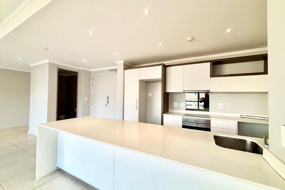 Modern open-plan kitchen featuring a large island with quartz countertops, built-in oven, electric hob, and sleek white cabinetry.