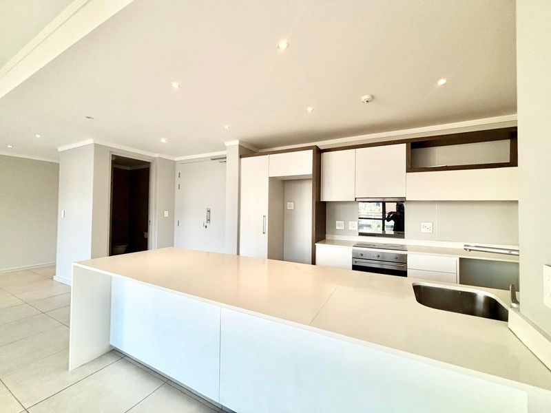 Modern open-plan kitchen featuring a large island with quartz countertops, built-in oven, electric hob, and sleek white cabinetry.