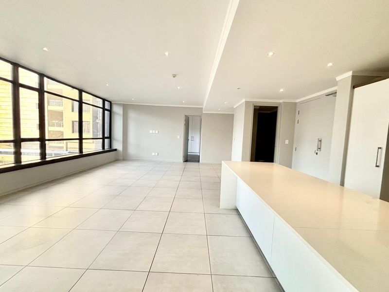 Spacious open-plan living area featuring large windows, modern tiled flooring, recessed lighting, and a sleek built-in kitchen island.