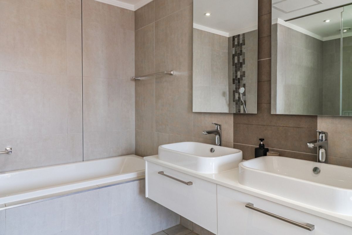 Modern bathroom featuring a double vanity with vessel sinks, chrome fixtures, large wall-mounted mirrors, and a clean tiled bathtub area.