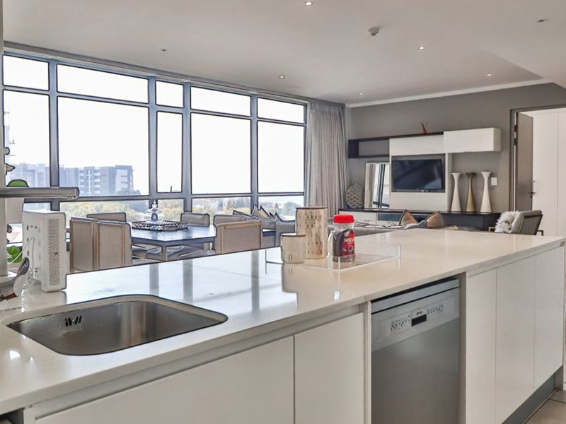 Modern open-plan living area featuring a sleek kitchen island with integrated appliances, expansive windows, and a seamless flow into the dining and lounge space.