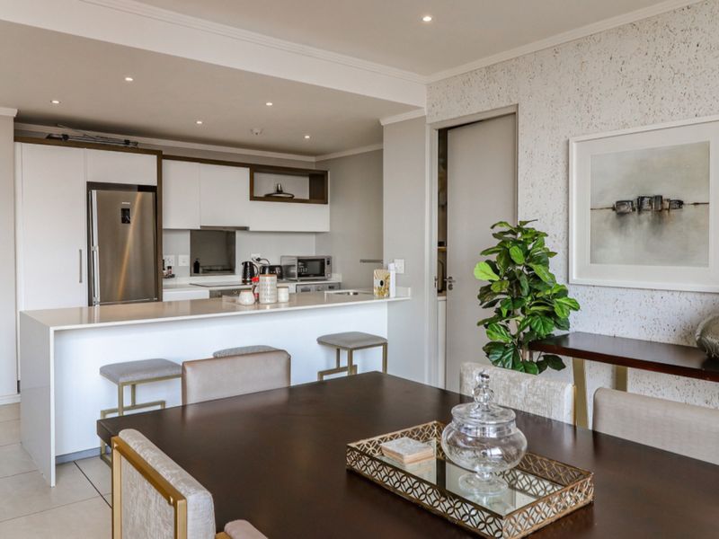 Modern open-plan living area featuring a sleek kitchen with a central island, quartz countertops, and high-quality built-in cabinetry, seamlessly flowing into the dining space.