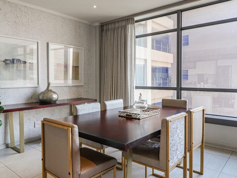 A bright dining area featuring large floor-to-ceiling windows, tiled flooring, and a textured feature wall, offering a modern and well-maintained space.