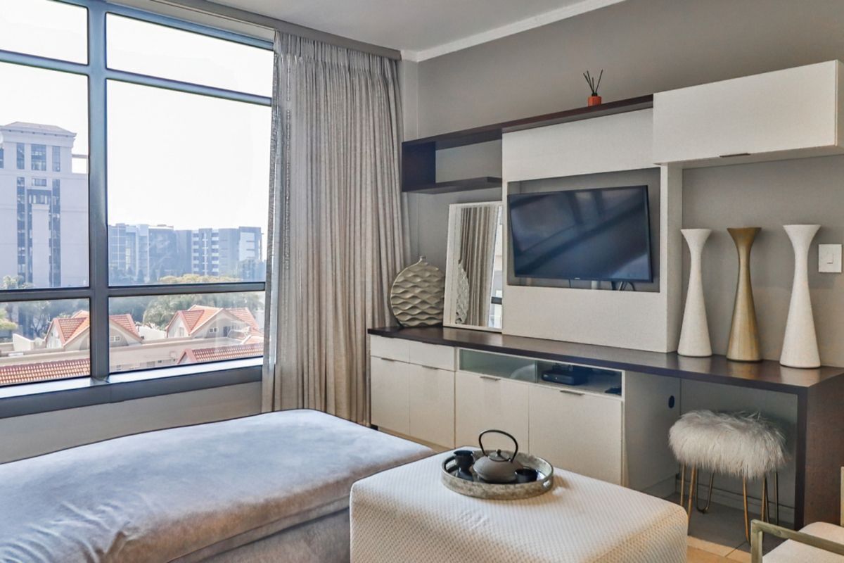 A modern living room featuring a large floor-to-ceiling window with urban views and a custom built-in media console with integrated shelving.