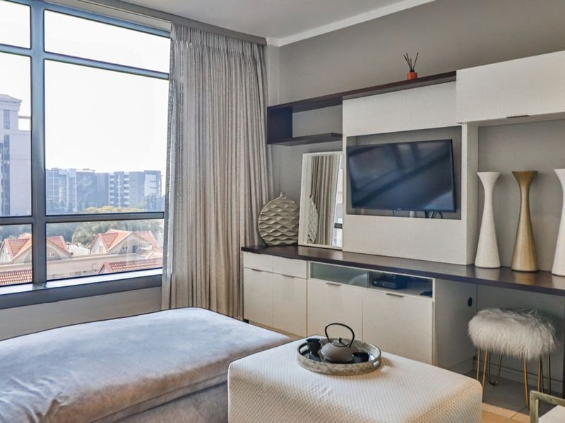 A modern living room featuring a large floor-to-ceiling window with urban views and a custom built-in media console with integrated shelving.