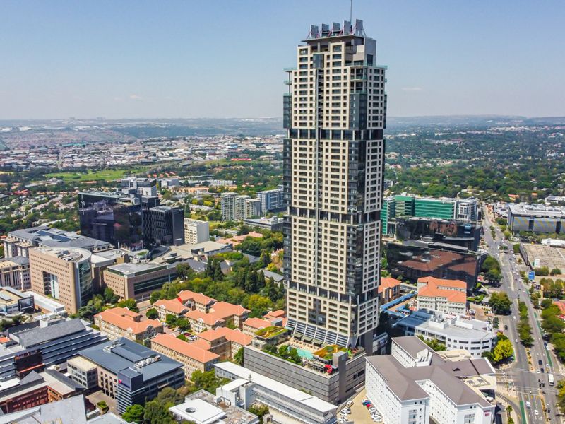 Aerial view of a modern high-rise apartment building situated in a dense urban landscape with surrounding commercial and residential infrastructure.