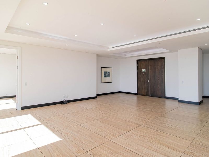 A spacious, empty living area featuring modern wood-look tiled flooring, recessed ceiling lighting, and double entry doors in a neutral, well-maintained setting.