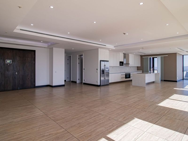 Spacious open-plan living and kitchen area featuring modern cabinetry, a central island, tiled flooring, and expansive floor-to-ceiling windows with natural light.