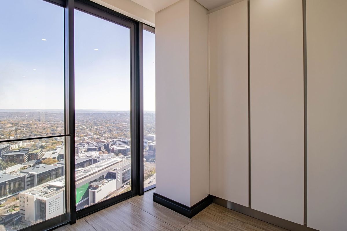 Modern bedroom featuring floor-to-ceiling windows with expansive city views and sleek, built-in floor-to-ceiling cupboards.